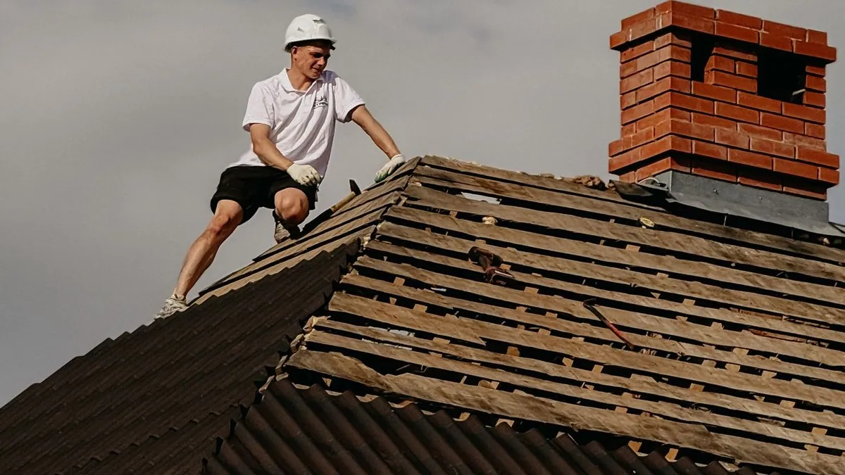 Worker repairing a tiled roof beside a brick chimney