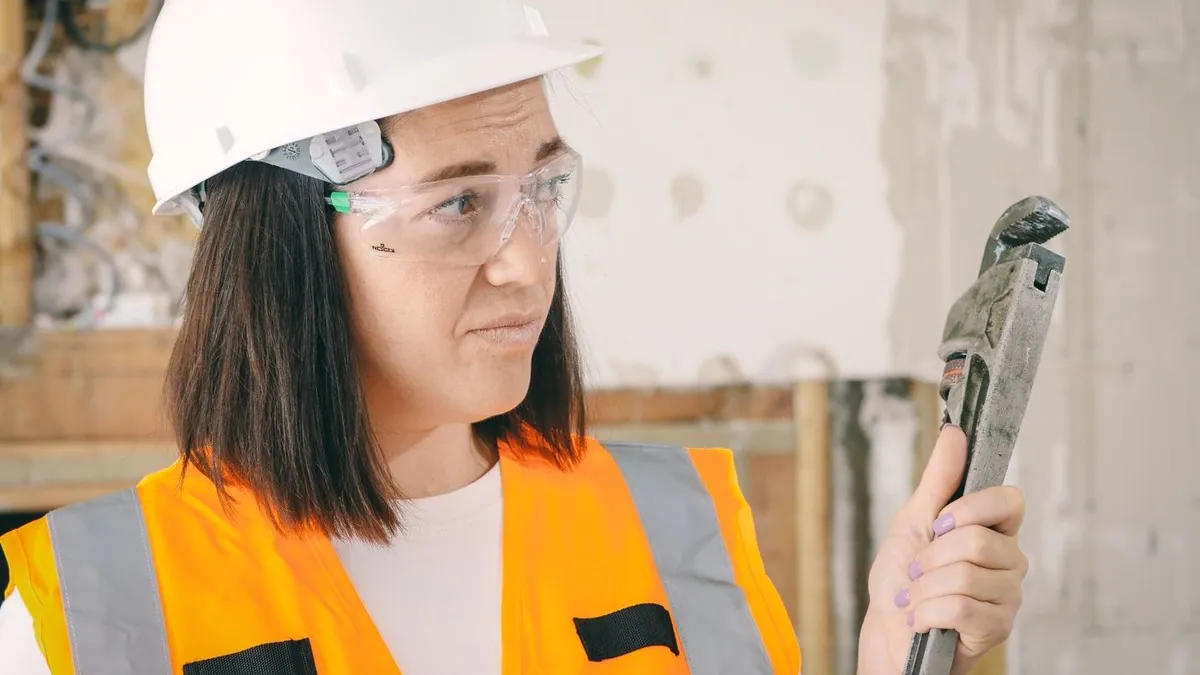 Worker wearing safety gear holding a pipe wrench during a renovation