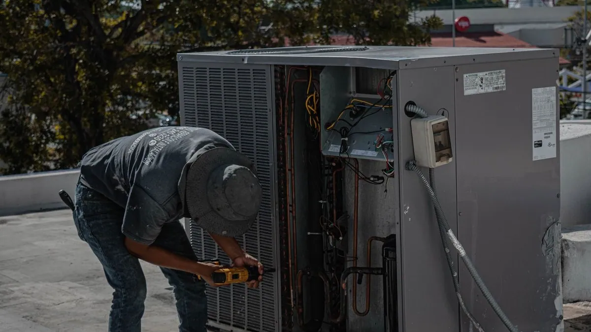 HVAC technician using a drill to repair an outdoor air-conditioning unit